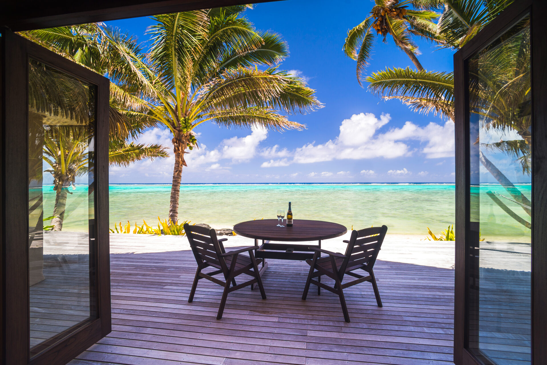 Cook Islands Landscape Travel Photography Luxury beachfront villa accommodation with sea views with champagne on a table next to tropical palm trees and the beautiful blue Pacific Ocean